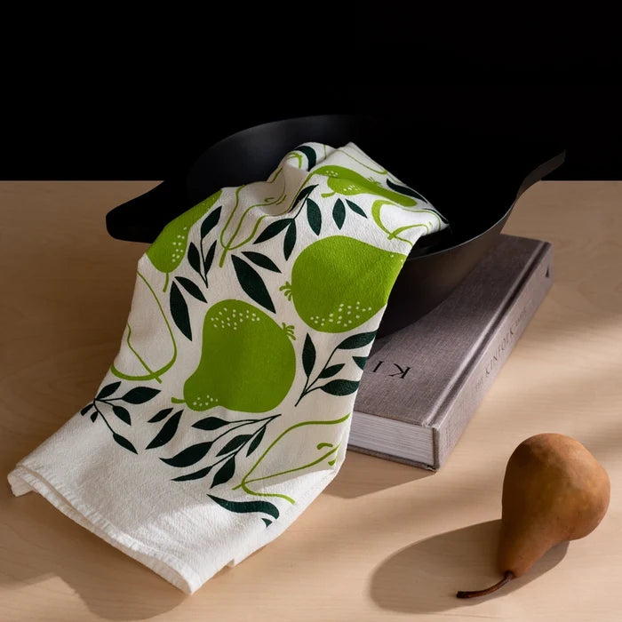 White towel with green pear design draped over a black bowl on a wooden surface.