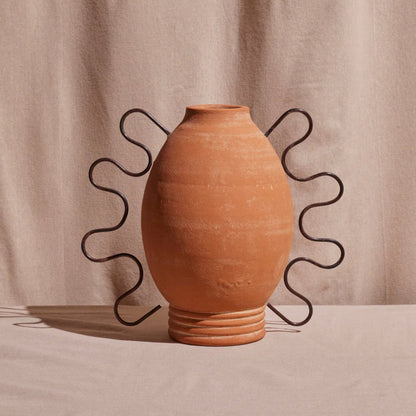 A terracotta amanda vessel with a sculptural design, featuring distinctive curved lines and hooks on the exterior.