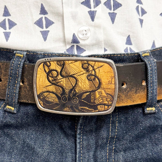Person wearing a patterned shirt and blue jeans with a decorative belt buckle featuring an octopus attacking a ship.