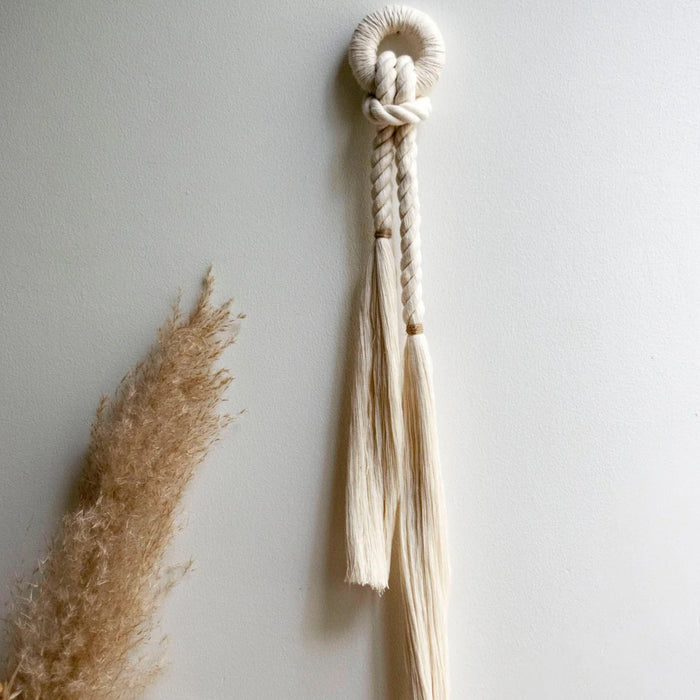 Handcrafted wall decor featuring natural cotton fiber rope with a color accent of jute, displayed against a neutral background with a tassel in the foreground.