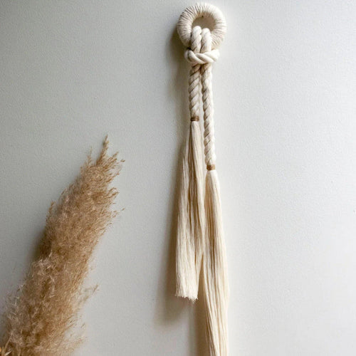 Handcrafted wall decor featuring natural cotton fiber rope with a color accent of jute, displayed against a neutral background with a tassel in the foreground.