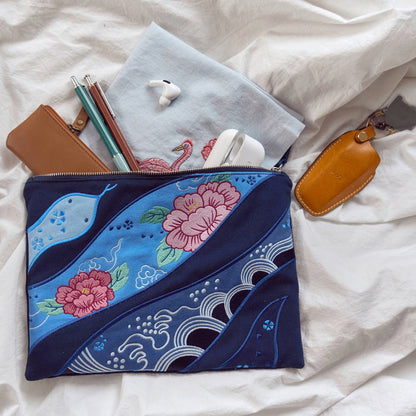 A navy-colored cotton pouch with floral and wave embroidery designs and a snake motif with everyday carry objects spilling out