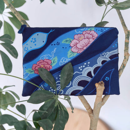 A navy-colored cotton pouch with floral and wave embroidery designs and a snake motif displayed in the branches of a house plant
