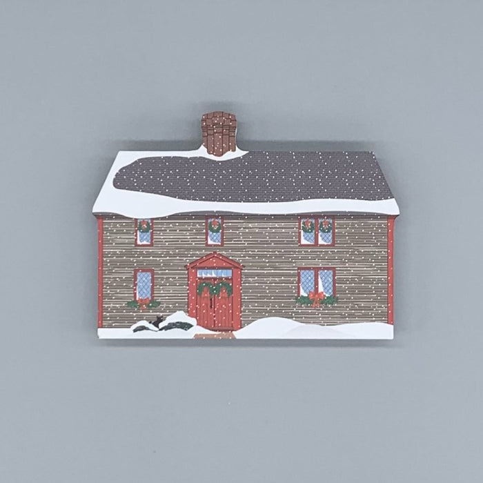 A decorative block featuring the Samuel Pickman House, depicted with a snowy roof and a red front door, against a grey background.