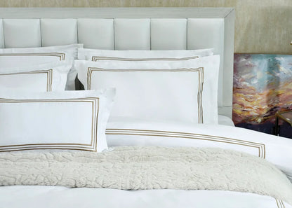 White duvet cover with gold-bordered shams and coordinating throw pillows