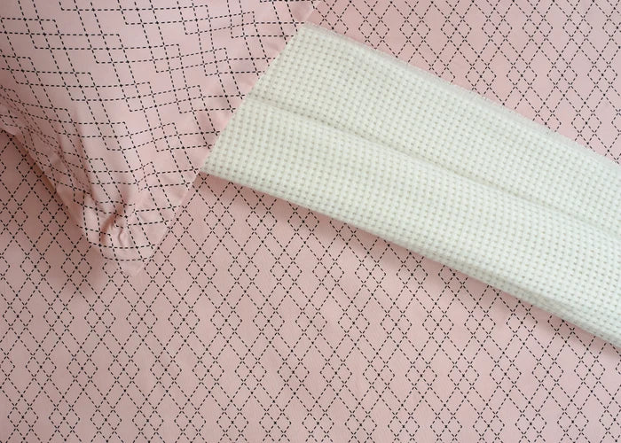 Pink diamond-pattern bed sheet detail with white woven trim