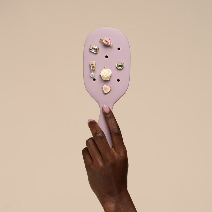 Purple paddle brush with various charms on a beige background