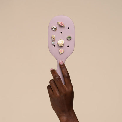 Purple paddle brush with various charms on a beige background