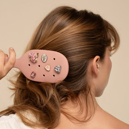 Person using a pink hairbrush with decorative clips in their hair against a beige background