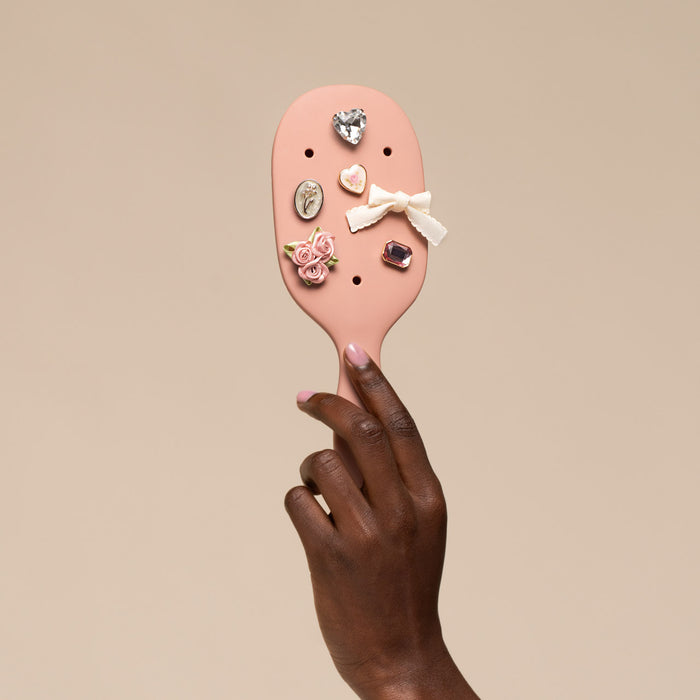 Pink hairbrush with decorative pins held by a hand against a beige background