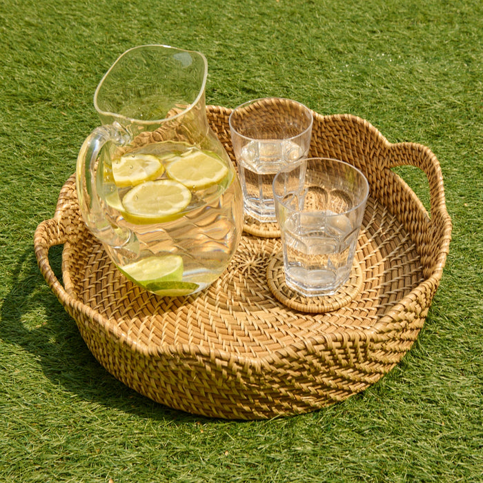 Wicker tray with a pitcher of lemon water and two glasses on a grassy background