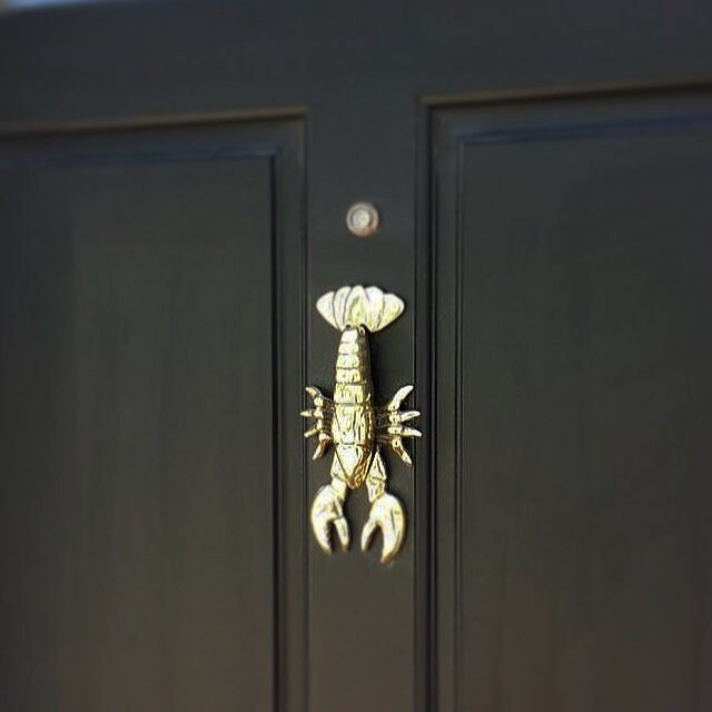 A brass door knocker in the shape of a lobster, with a highly polished finish mounted on a black door