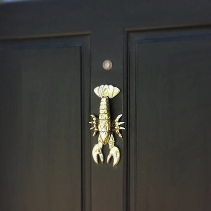 A brass door knocker in the shape of a lobster, with a highly polished finish mounted on a black door