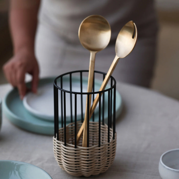 Two gold spoons in a metal and rattan utensil holder