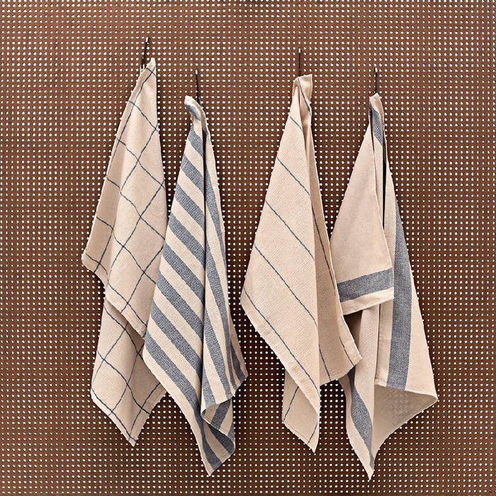 A set of four folded striped kitchen towels in natural and blue denim colors, hanging on a wall.