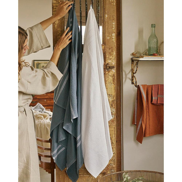 Person hanging towels on a rack with a rustic wooden door and shelf in the background.