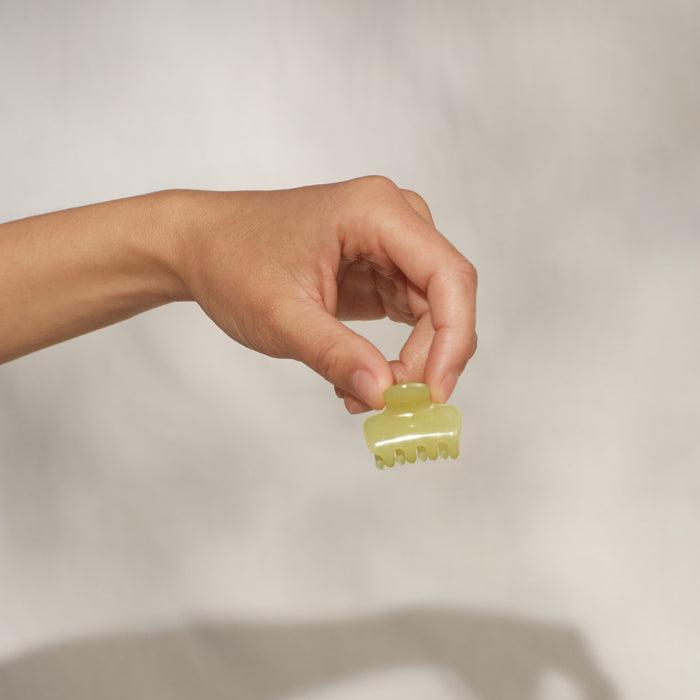 Hand holding single KITSCH Butter Yellow Jelly Cloud Clip Mini between fingers — close-up detail shot on cream background — mini claw clip design, jelly texture in butter yellow — All-Day Hold, Made from Recycled Materials — KITSCH Pearlized Cream & Butter Yellow Jelly Cloud Clips Mini 8pcs