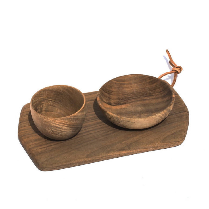 A rectangular cutting board made of walnut wood, accompanied by two wooden bowls, placed on a white background with a rope handle.