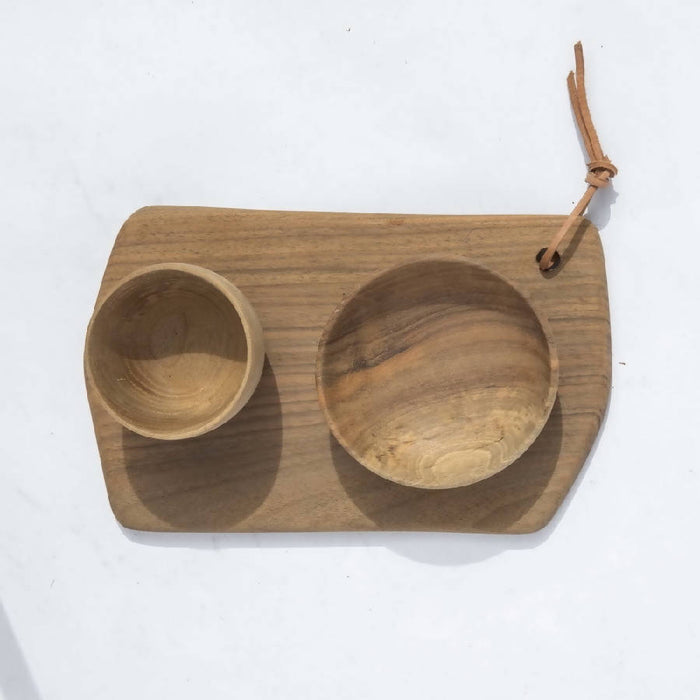 A rectangular cutting board made of walnut wood, accompanied by two wooden bowls, placed on a white background with a rope handle.