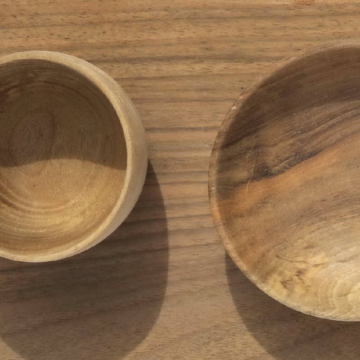 A rectangular cutting board made of walnut wood, accompanied by two wooden bowls, placed on a white background with a rope handle.