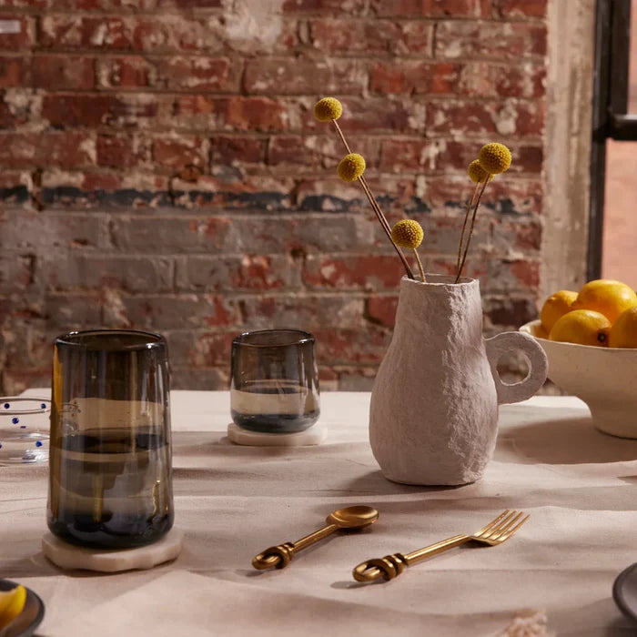 Two clear glasses with a smoke-like pattern on the surface, displayed on a table with a vase of dried flowers.