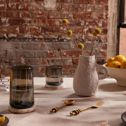 Two clear glasses with a smoke-like pattern on the surface, displayed on a table with a vase of dried flowers.