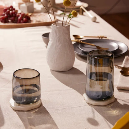 Smoke and Luster Recycled Glassware on a table with a vase of dried flowers.