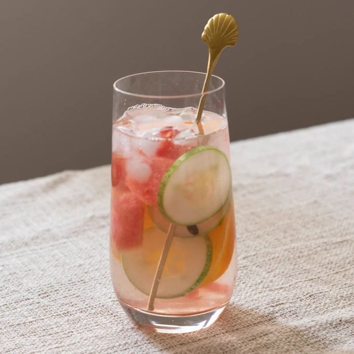 Glass of iced cocktail with fruit and a gold stirrer on a textured surface