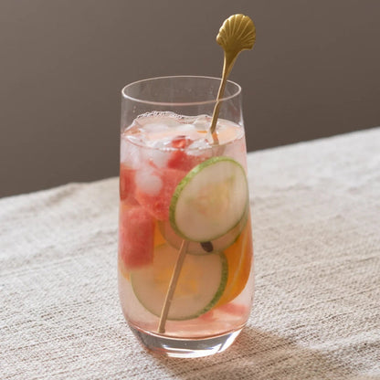 Glass of iced cocktail with fruit and a gold stirrer on a textured surface