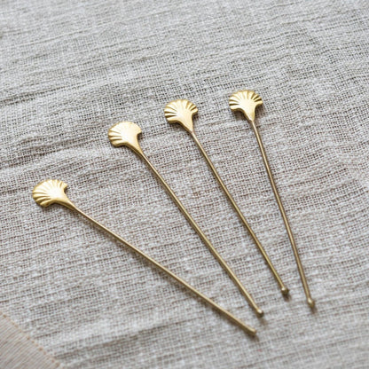 Set of four gold stirrers with shell designs on a textured gray surface