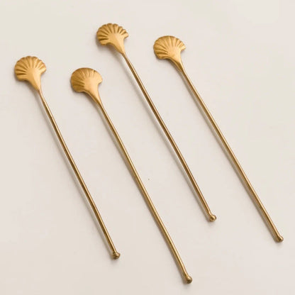 Set of four gold shell-shaped stirrers on a light beige background