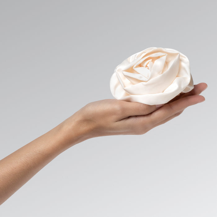 Hand holding a cream satin rosette clip against a gray background