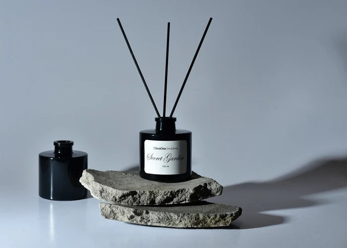 Reed diffuser bottle with black glass, four fragrance reeds, and stone base.