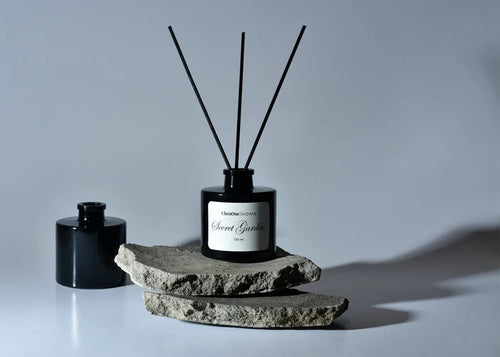 Reed diffuser bottle with black glass, four fragrance reeds, and stone base.