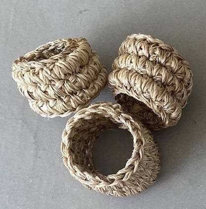 Three beige handwoven napkin rings on a grey concrete background.