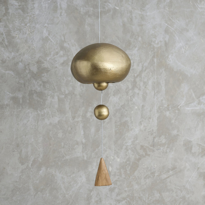 Brass and wooden hanging bell against a gray concrete wall