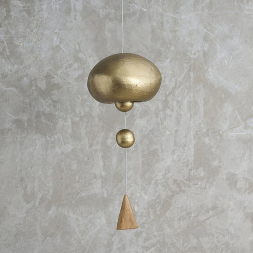 Brass and wooden hanging bell against a gray concrete wall