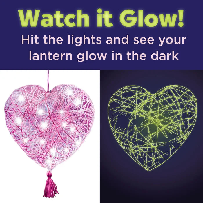 Heart-shaped lantern with pink string lights on the left and glowing green string pattern on the right against a dark background.