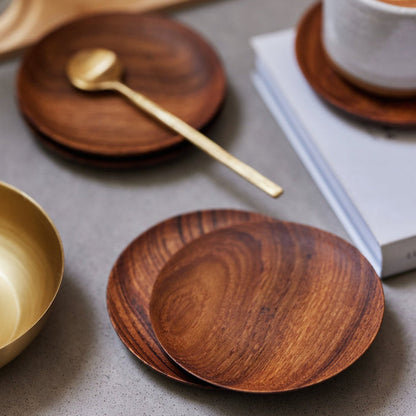 A set of teak wood coasters with a brass spoon and a white mug.