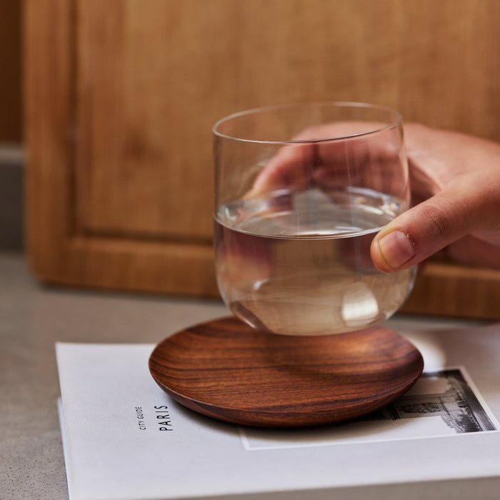 A hand placing a clear glass on a teak wood coaster.