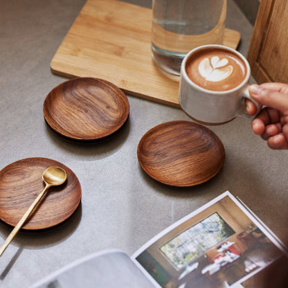 A set of teak wood coasters with a brass spoon and a white mug filled with coffee.