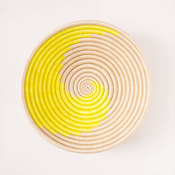 Round woven basket with yellow and beige spiral pattern on a white background
