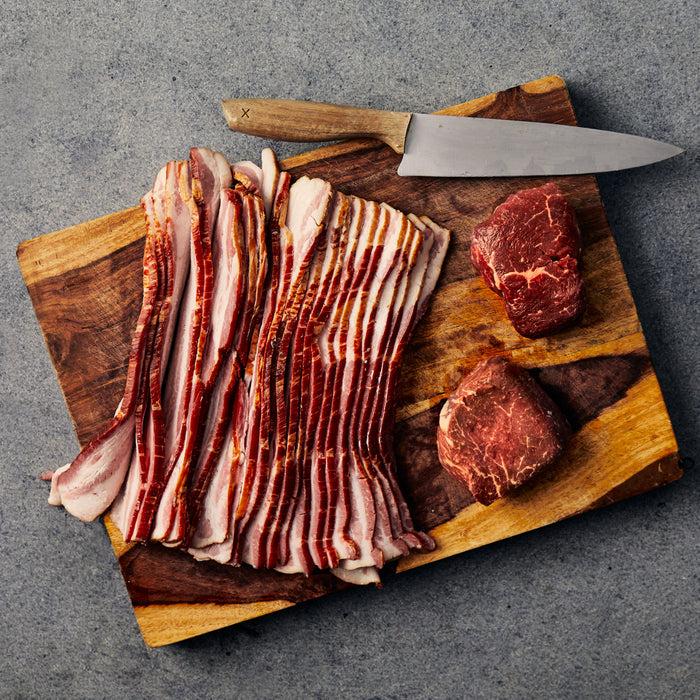 Raw bacon and beef on a wooden cutting board with a knife against a gray background