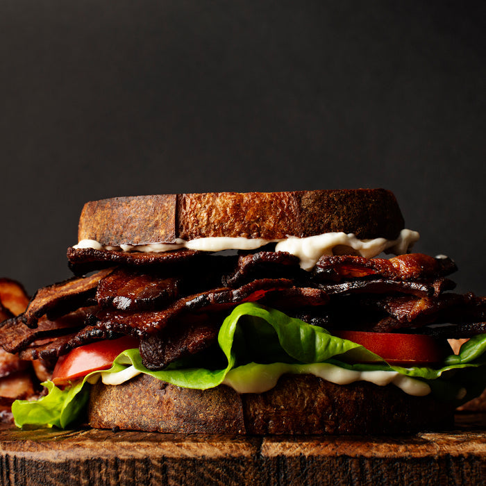 Deluxe sandwich with bacon, lettuce, and tomato on a wooden board against a dark background
