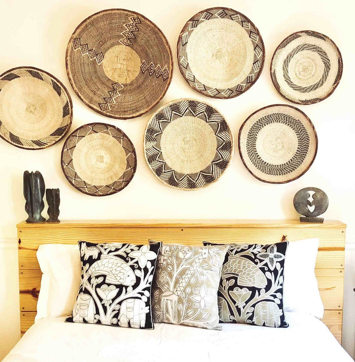 An assortment of round, beige-colored woven basket with a geometric pattern and a coiled rim hanging on a wall above a bed.