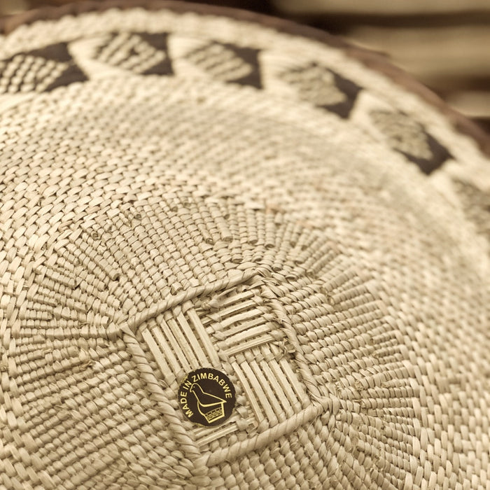A round, beige-colored woven basket with a geometric pattern and a coiled rim.