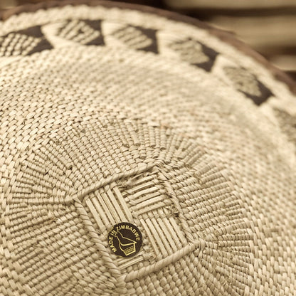 A round, beige-colored woven basket with a geometric pattern and a coiled rim.