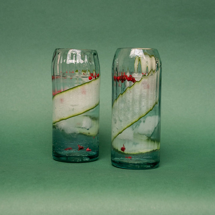 Two clear hand-blown glasses filled with liquid and garnish.