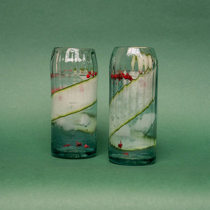 Two clear hand-blown glasses filled with liquid and garnish.