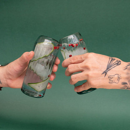 Two hands holding a clear hand-blown glass filled with liquid and garnish